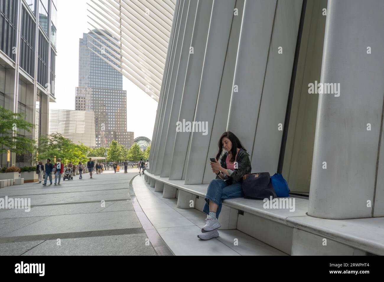 USA, New York, City, donna seduta all'edificio Oculus e con il cellulare, skyline urbano alle spalle Foto Stock