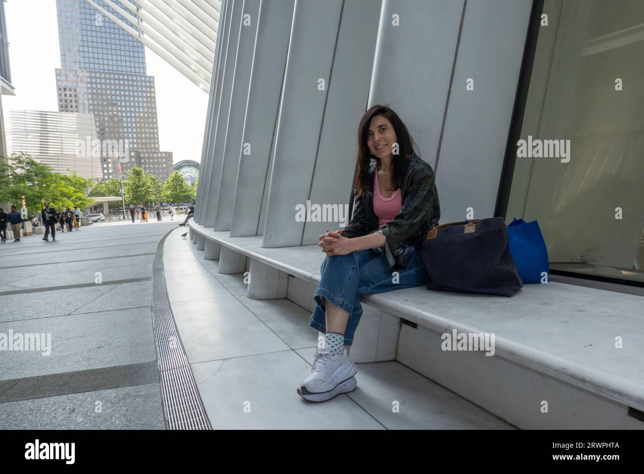 USA, New York, City, donna seduta all'edificio Oculus e con il cellulare, skyline urbano alle spalle Foto Stock