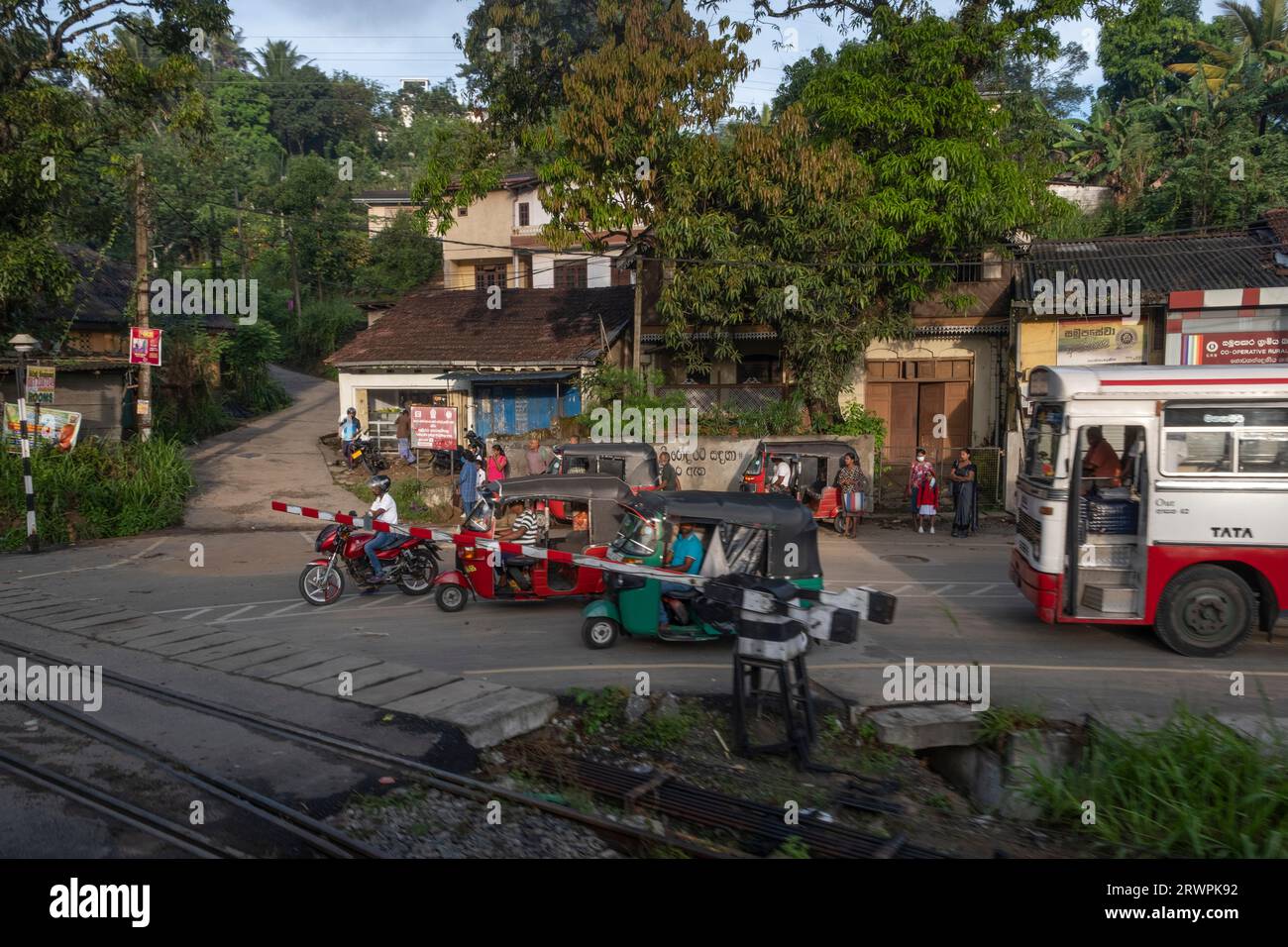 Sri Lanka. Passaggio a livello (passaggio in treno); rickshaw (tuk-tuk) taxi & tuk-tuk rank & bus; ferrovia da Kandy a Kadugannawa, vicino a Henawala Danthure Road Foto Stock