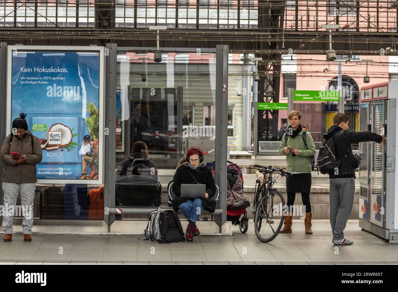 Foto di una donna che lavora sul suo portatile, a distanza, dalla piattaforma della stazione ferroviaria di Koln Hbf a Colonia, Germania. Köln Hauptbahnhof o Colog Foto Stock