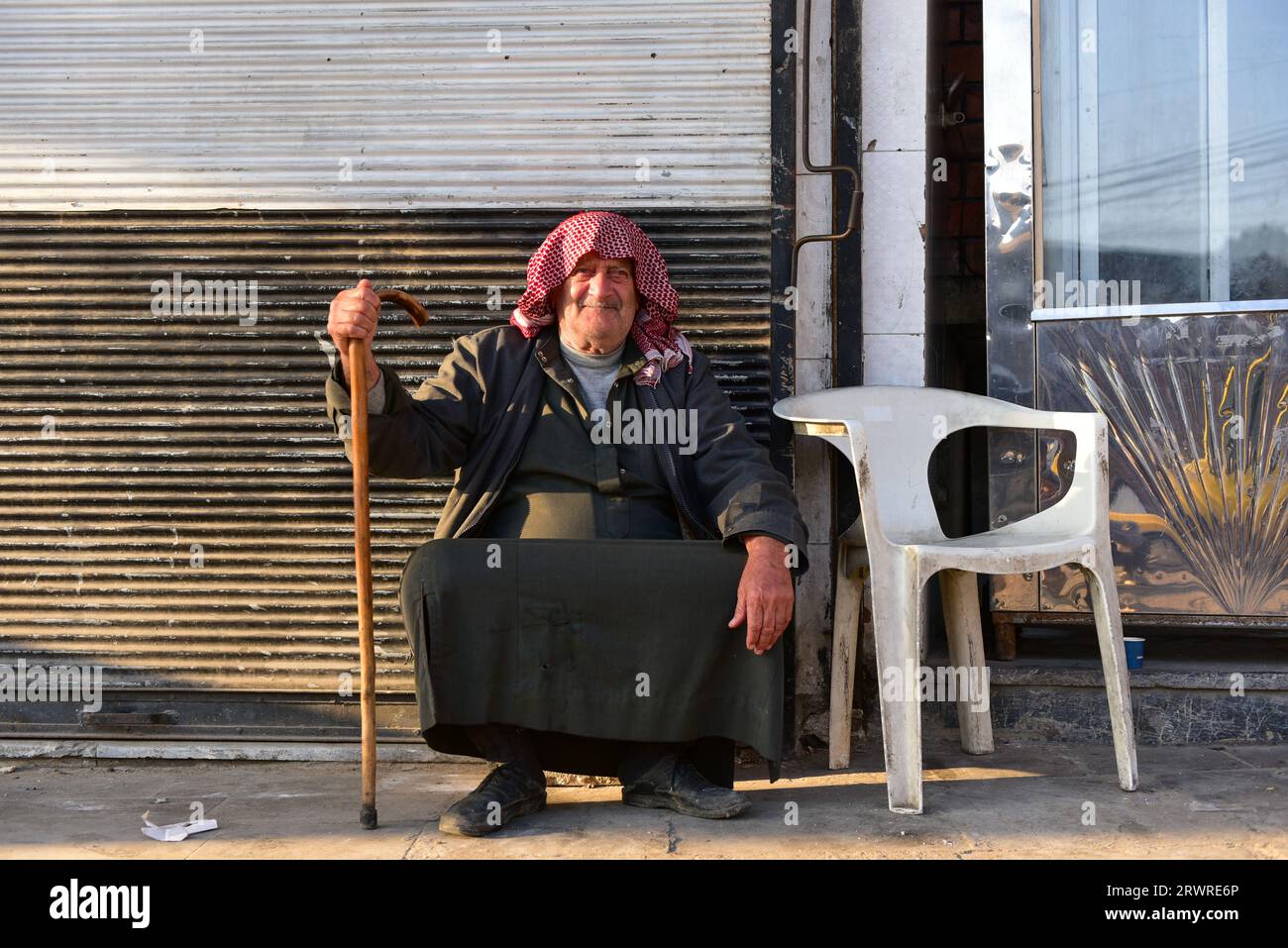 Un uomo del posto a Keffiyeh che tiene una canna fuori da un grande negozio che vendeva sapone di Aleppo, sedeva tranquillamente sotto il sole del tramonto Foto Stock