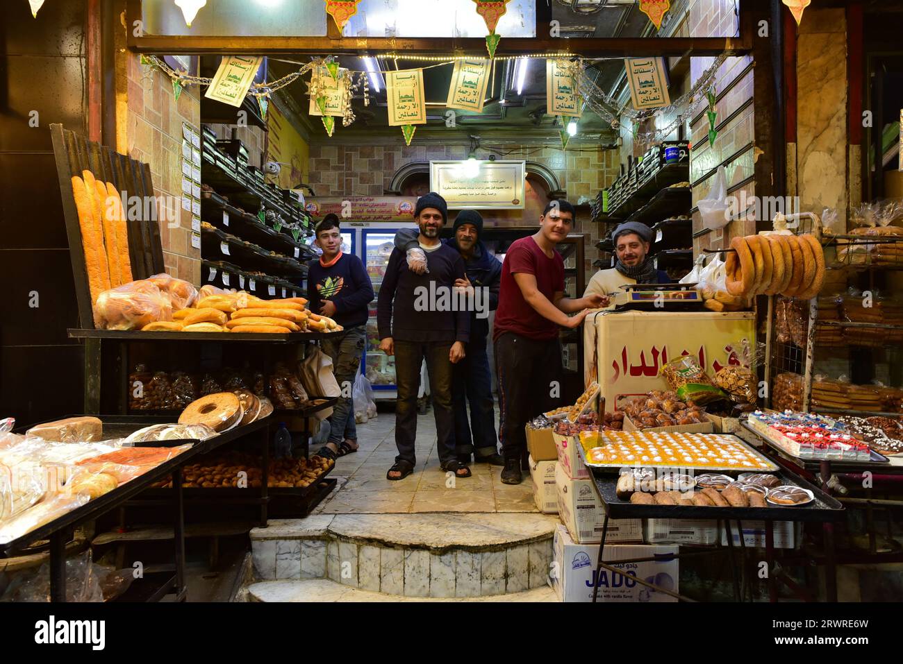 Un gruppo di uomini del posto, pane e dolci in un negozio ad Aleppo, in Siria, in prima serata. Foto Stock