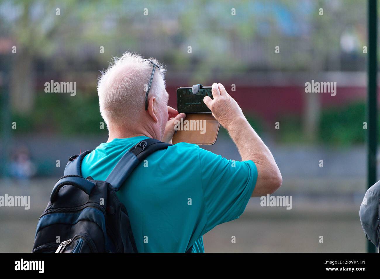 Uomo anziano che usa lo smartphone per scattare foto all'aperto indossando uno zaino in una giornata di sole a Melbourne, Australia. Foto Stock