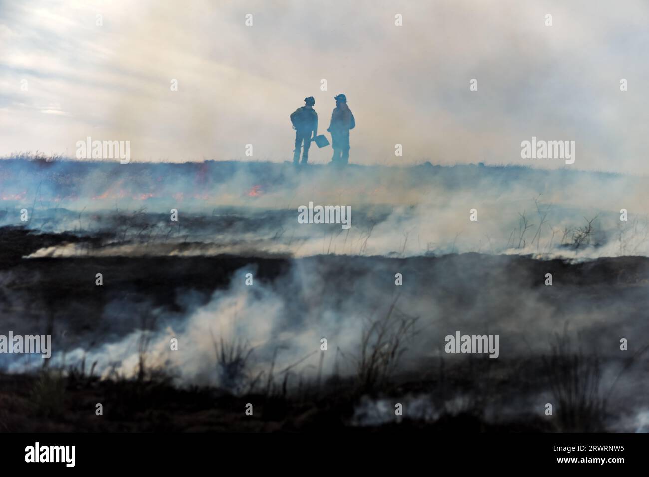 Due vigili del fuoco si stagliano in fumo su una collina in fiamme dopo un incendio Foto Stock