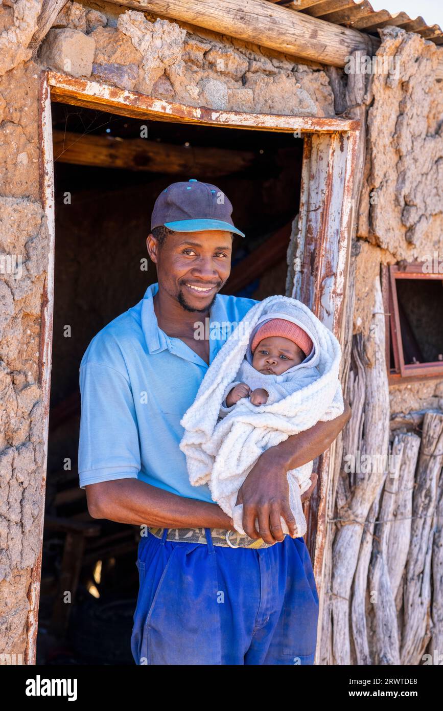 villager uomo africano adulto, genitore single, che tiene il bambino davanti alla baracca, villaggio in Botswana, Foto Stock