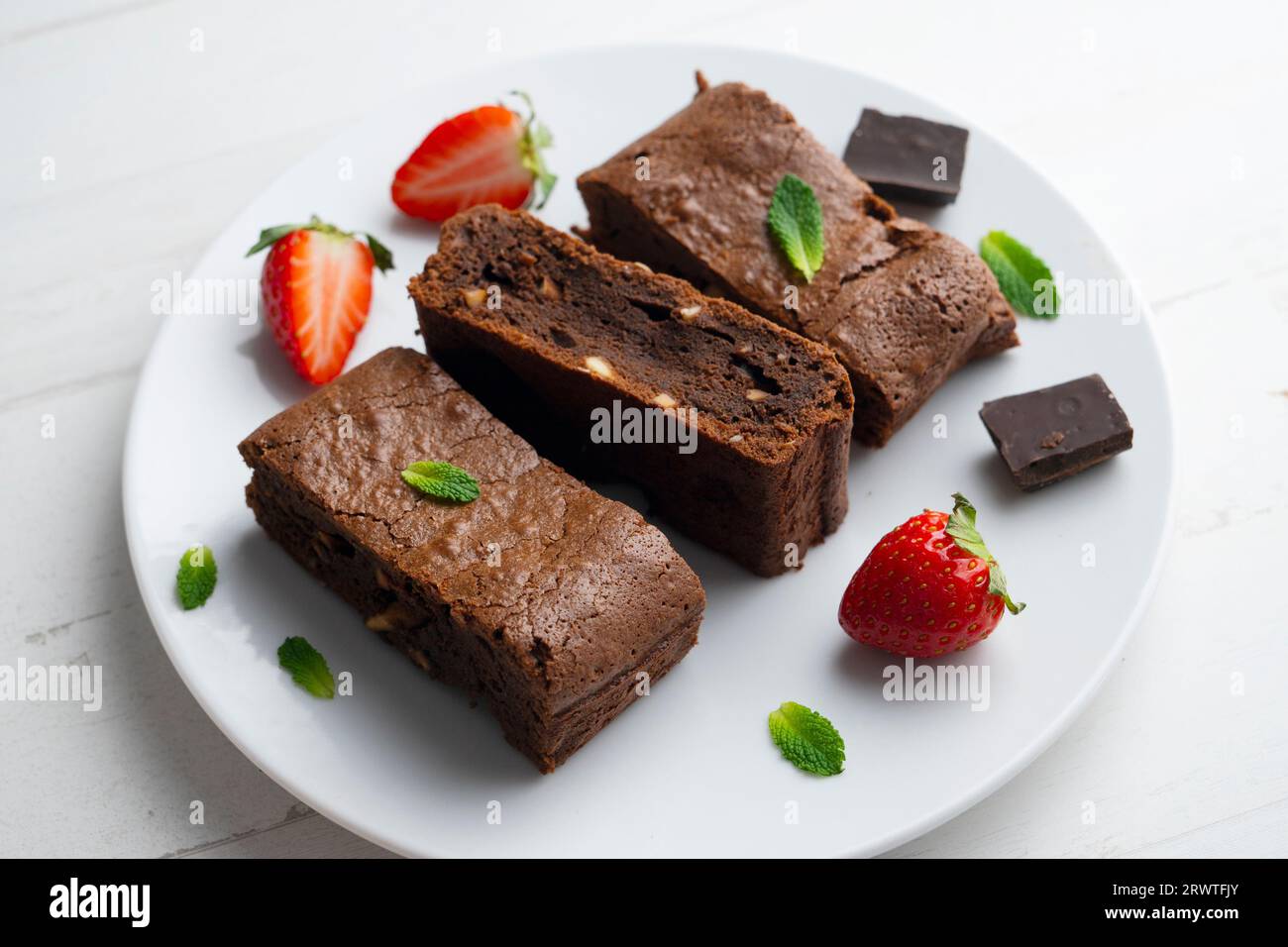 Brownie al cioccolato tagliato a porzioni e decorato con fragole e menta. Foto Stock