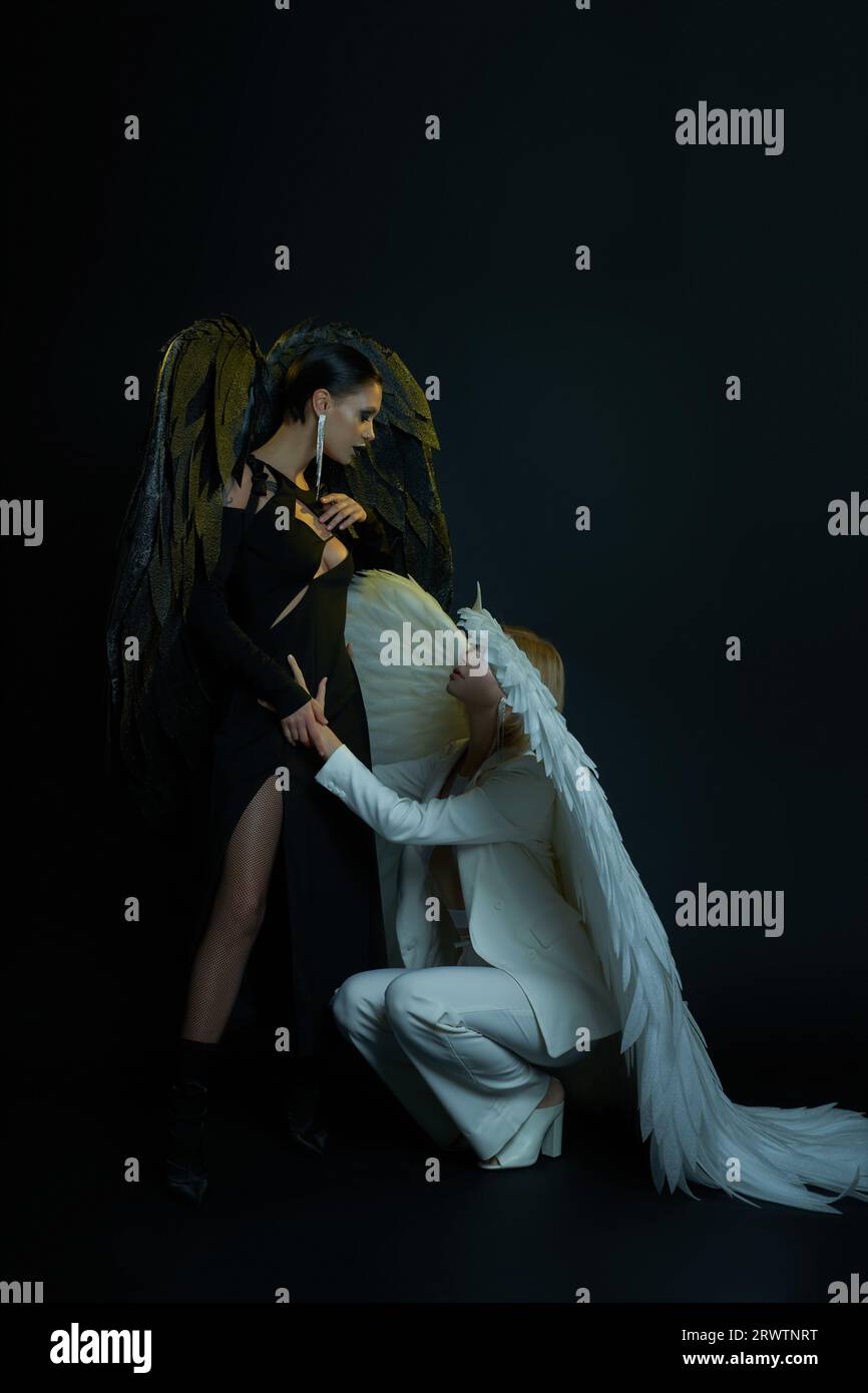 Angelo celeste che tiene per mano un demone oscuro in piedi su sfondo nero, donne in costumi di Halloween Foto Stock