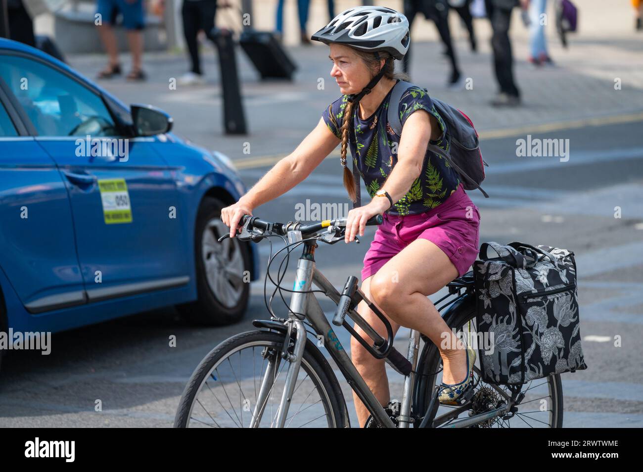 Donna o donna di mezza età in bicicletta o in bicicletta. Ciclista donna che indossa un casco di sicurezza e uno zaino con borse portabagagli nel Regno Unito. Foto Stock