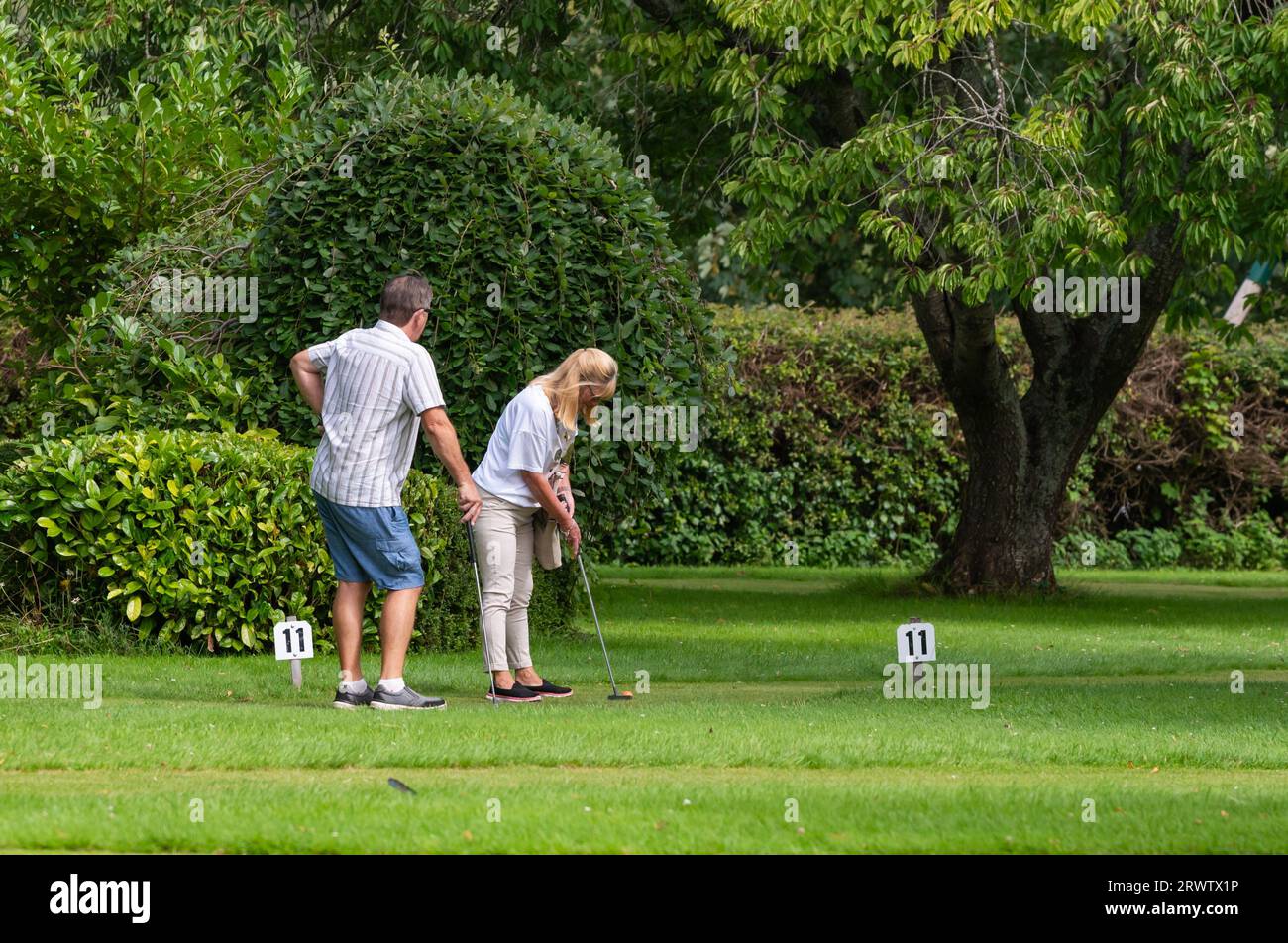 Uomo e donna di mezza età, presumibilmente una coppia, giocando a putting o a golf pazzo su un putting green in erba in estate nel Regno Unito. Foto Stock