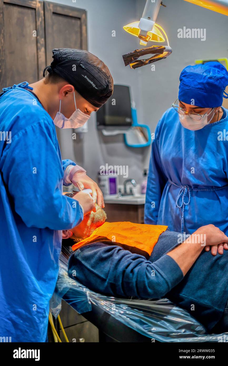 Due professionisti medici in scrub stanno eseguendo una procedura su un paziente in una sala operatoria dell'ospedale Foto Stock