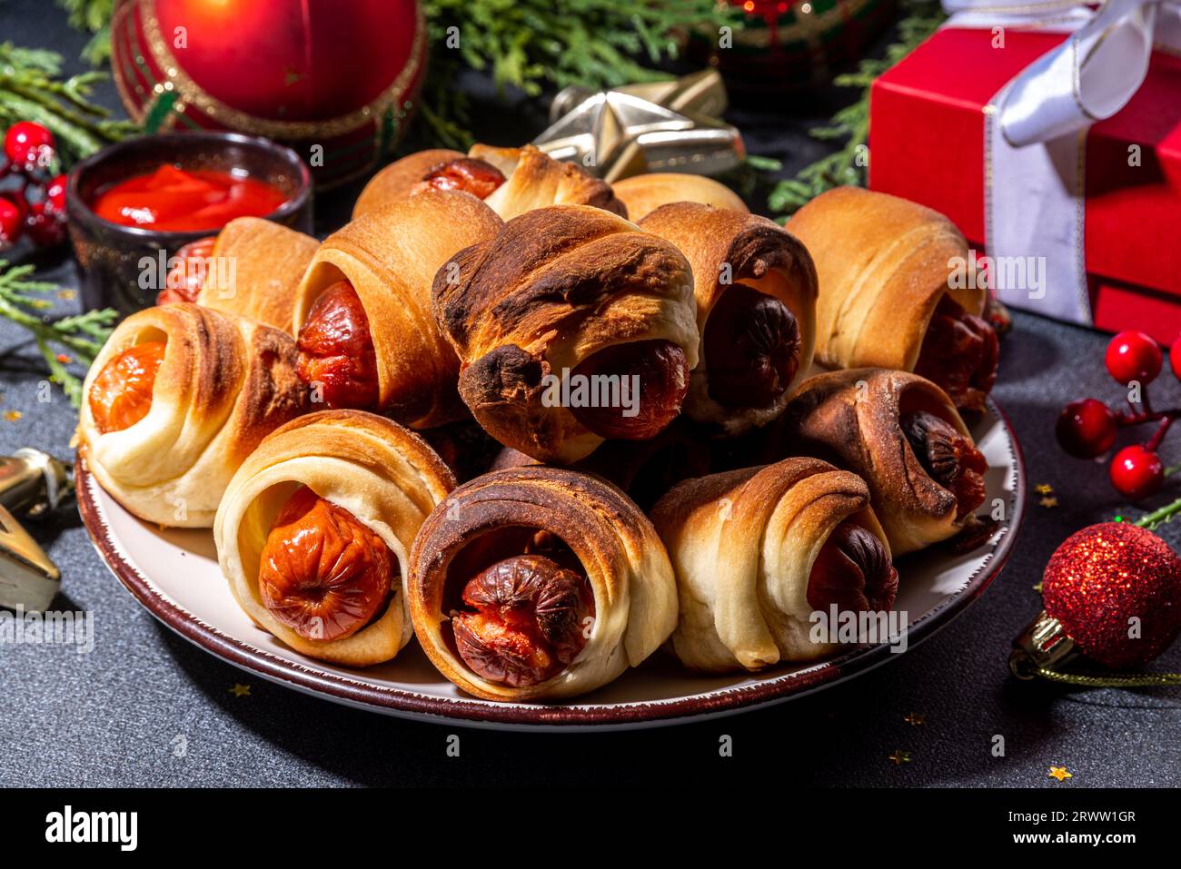 Piatto di Natale tradizionale ricetta maiali in coperte, salsicce avvolti in pancetta, forno di pasta sfoglia hot dog panini con rami d'albero di Natale, decorati Foto Stock