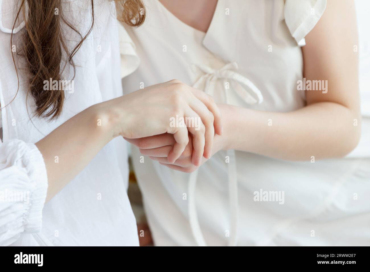 Due ragazze, vestite di bianco, si toccano la mano a vicenda. Parte del corpo. Messa a fuoco delle dita Foto Stock
