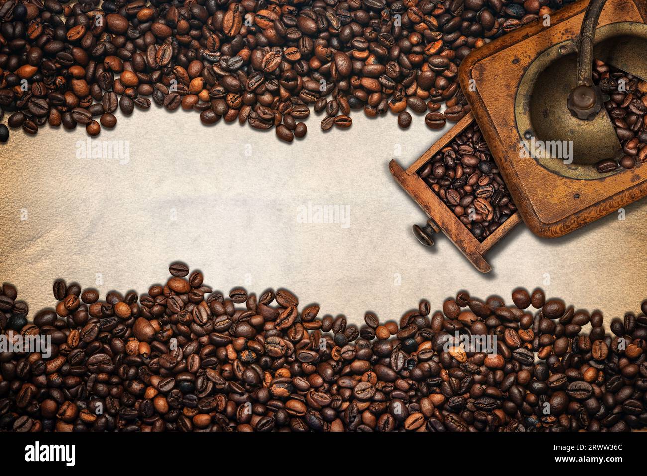 Grande gruppo di chicchi di caffè tostati e un macinacaffè manuale su pergamena vuota con spazio per le copie. Composizione orizzontale. Foto Stock