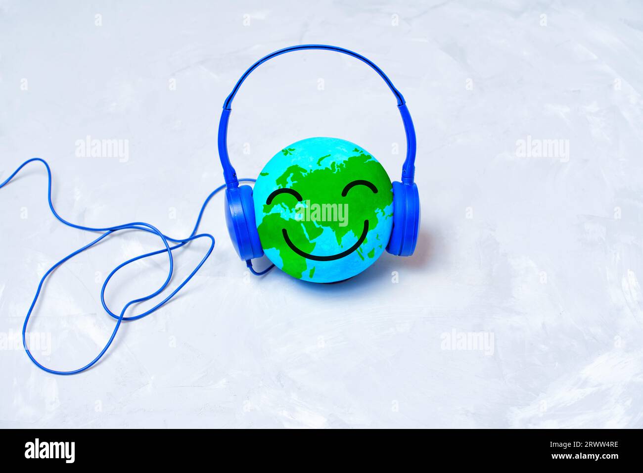 Globo sorridente immerso nell'ascolto con cuffie blu isolate su uno sfondo di cemento. Concetto di scoperta musicale internazionale. Foto Stock