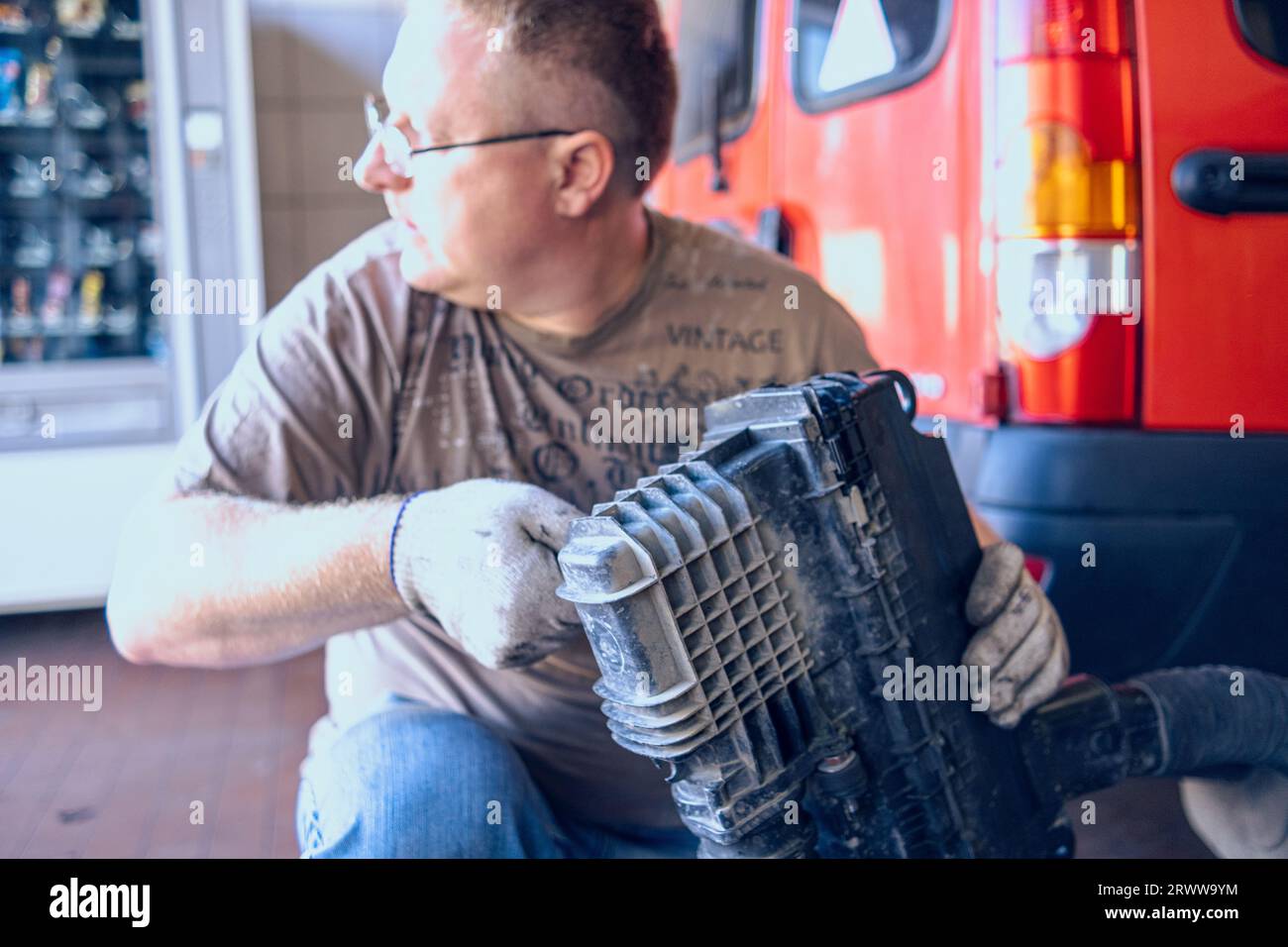 Un uomo con gli occhiali mantiene un'auto in un garage. Riparazione auto effettuata da uno specialista esperto in un'officina di riparazione auto. Sostituzione dell'olio e del filtro nella vettura. Foto Stock
