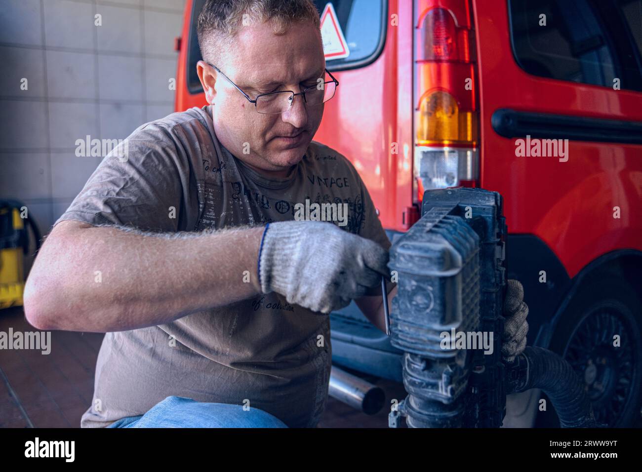Un uomo con gli occhiali mantiene un'auto in un garage. Riparazione auto effettuata da uno specialista esperto in un'officina di riparazione auto. Sostituzione dell'olio e del filtro nella vettura. Foto Stock