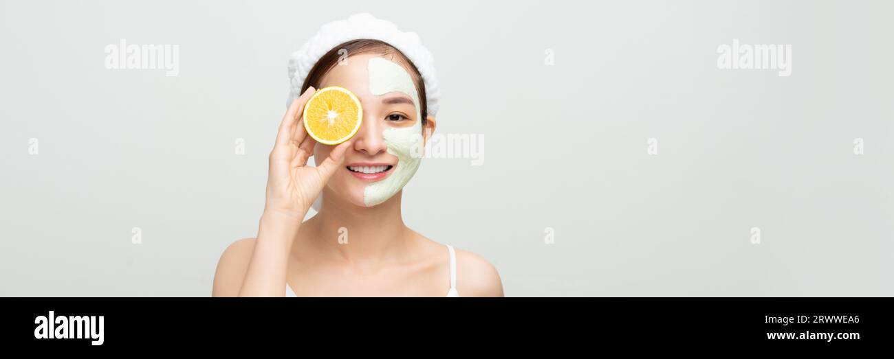 Giovane donna con maschera di argilla facciale che tiene fetta di frutta arancia che copre gli occhi. Banner Foto Stock