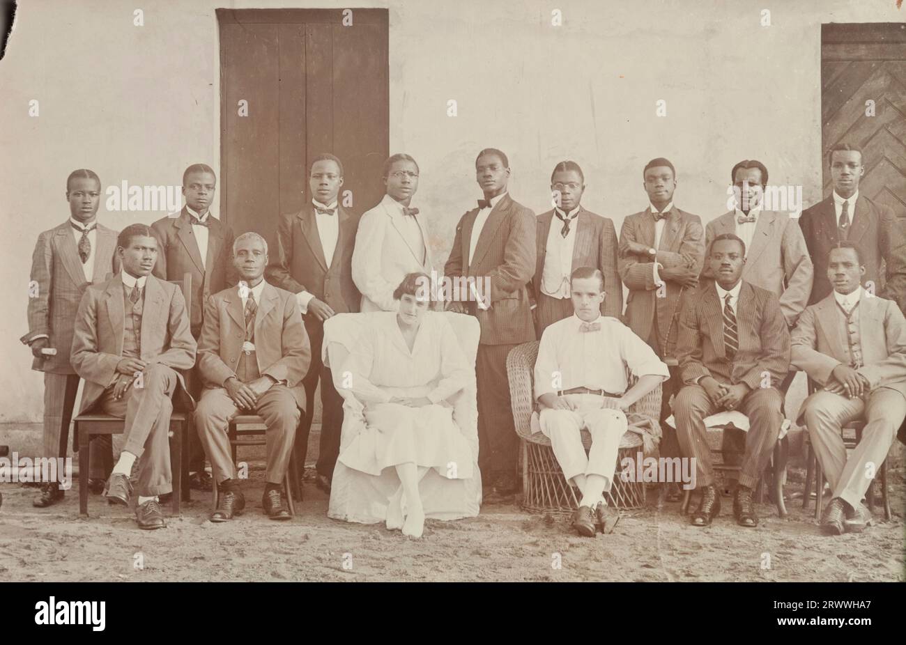 Fotografia formale di gruppo del personale d'ufficio presumibilmente della African and Eastern Trade Corporation, costituita nel 1919 dalla fusione di Swanzy's, Millers Ltd e l'African Association. 13 uomini africani vestiti in modo intelligente posano per la telecamera con il signor e la signora Tamlin seduti al centro. Didascalia del testo originale: Office staff maggio 1920. Metà Assinie. Foto Stock