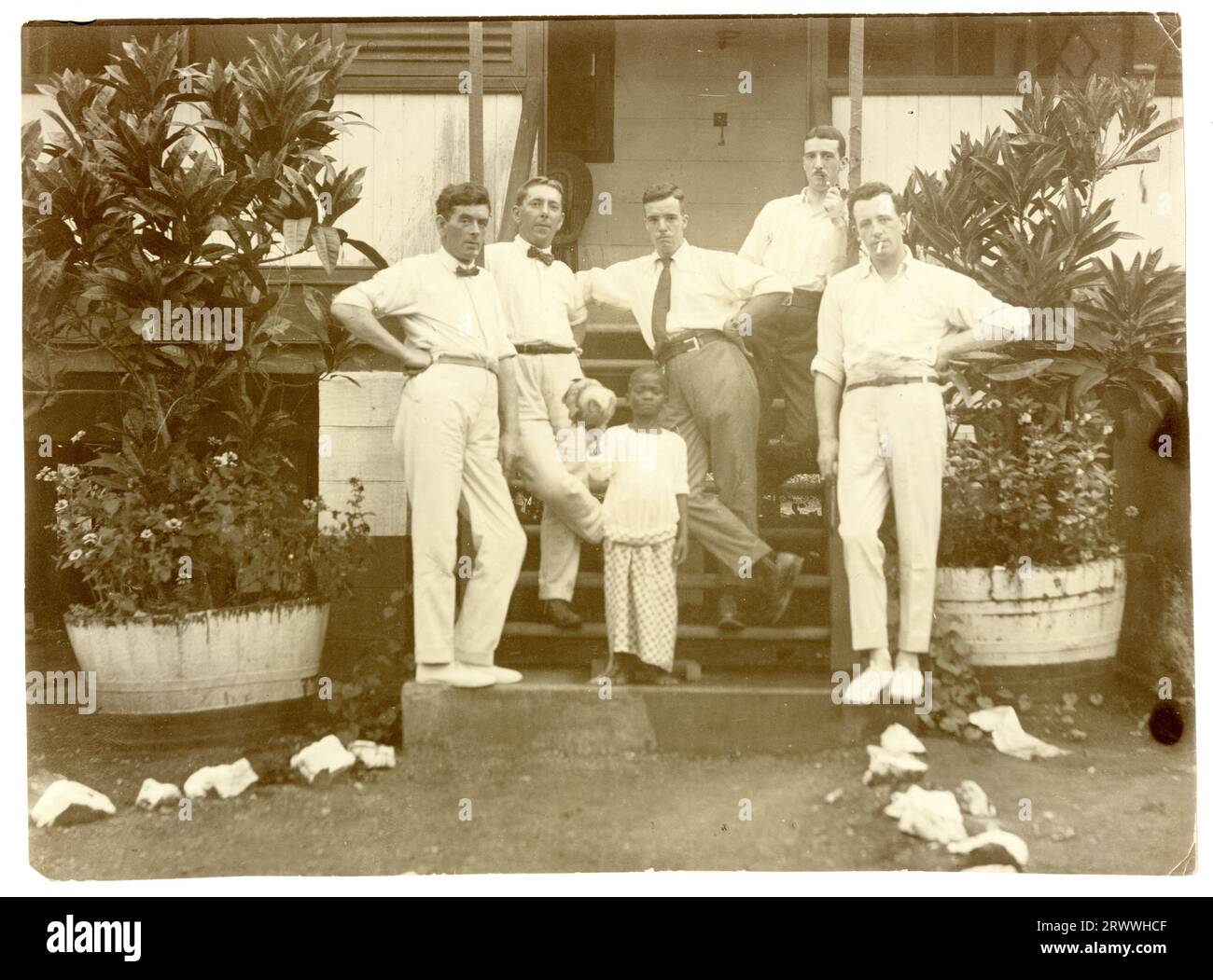 Alfred Tamlin si erge con quattro colleghi sui gradini del bungalow Millers, un grande edificio in pietra con piante in vaso all'esterno. Un bambino africano è con loro. Didascalia del manoscritto originale: Millers bungalow, Nsawam, Gold Coast 20/5/18. P. Kane, J.R. Small, A.E. Tamlin, Morris, McDonald. Didascalia manoscritta successiva: Alfred Tamlin Centre. Foto Stock