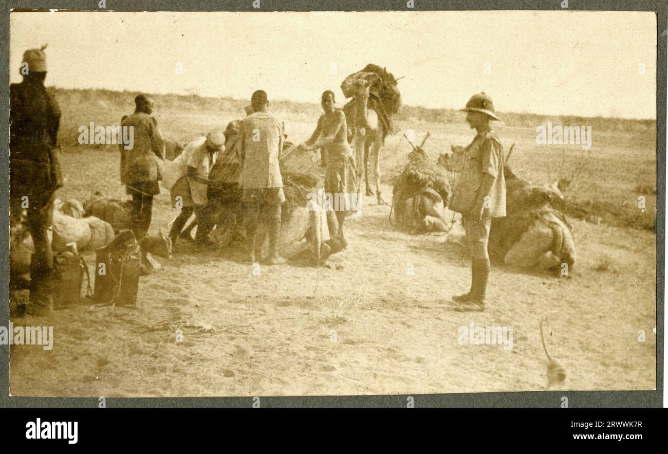 Una delle tre foto di un C.N. Jones a Jubaland, ora parte della Somalia, probabilmente durante la prima guerra mondiale. Questa immagine mostra gli uomini africani che caricano i cammelli con i pacchi. Il signor Jones li guarda lavorare, indossando un'uniforme tropicale dell'esercito e un elmetto Pith. Didascalia pagina originale: C.N.Jone's [sic] in Juba Land. Africa orientale. Foto Stock