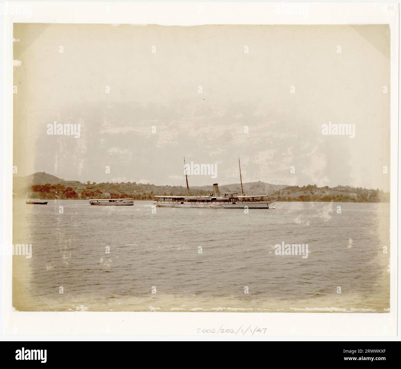 Vista di una nave a due alberi con un unico imbuto, con un ponte a baldacchino in mare. Ci sono colline di pianura sullo sfondo e due barche più piccole a sinistra. La didascalia scritta a mano recita: R.I.M.S. Elphinestone. Foto Stock