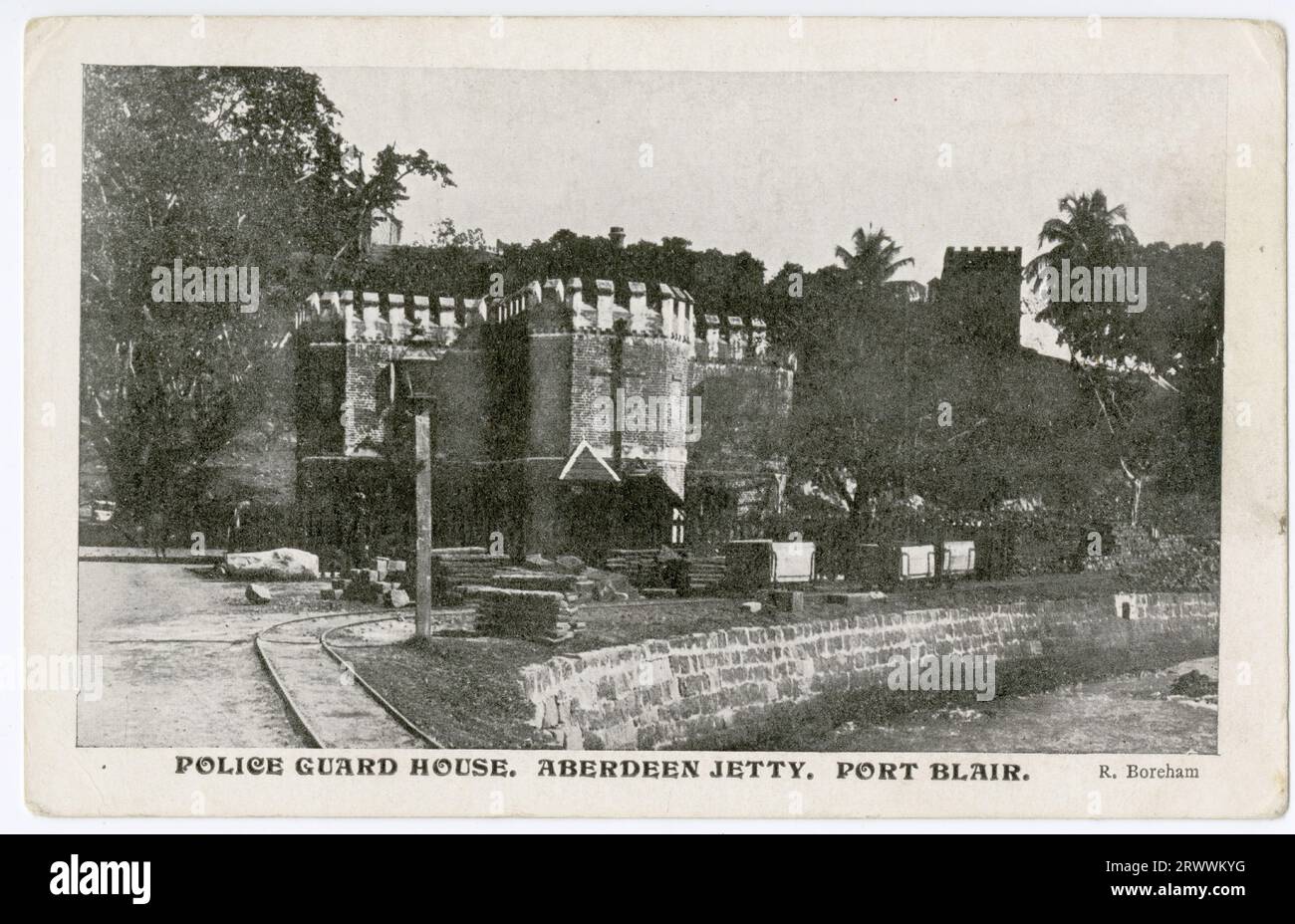 Cartolina che mostra una struttura tipo castello, che incorpora un parapetto a castellatura, descritta in una didascalia stampata come Police Guard House, Aberdeen Jetty, Port Blair. L'edificio è situato adiacente ad un molo in pietra, dotato di una linea ferroviaria su cui sono stazionati alcuni carri carichi. Foto Stock