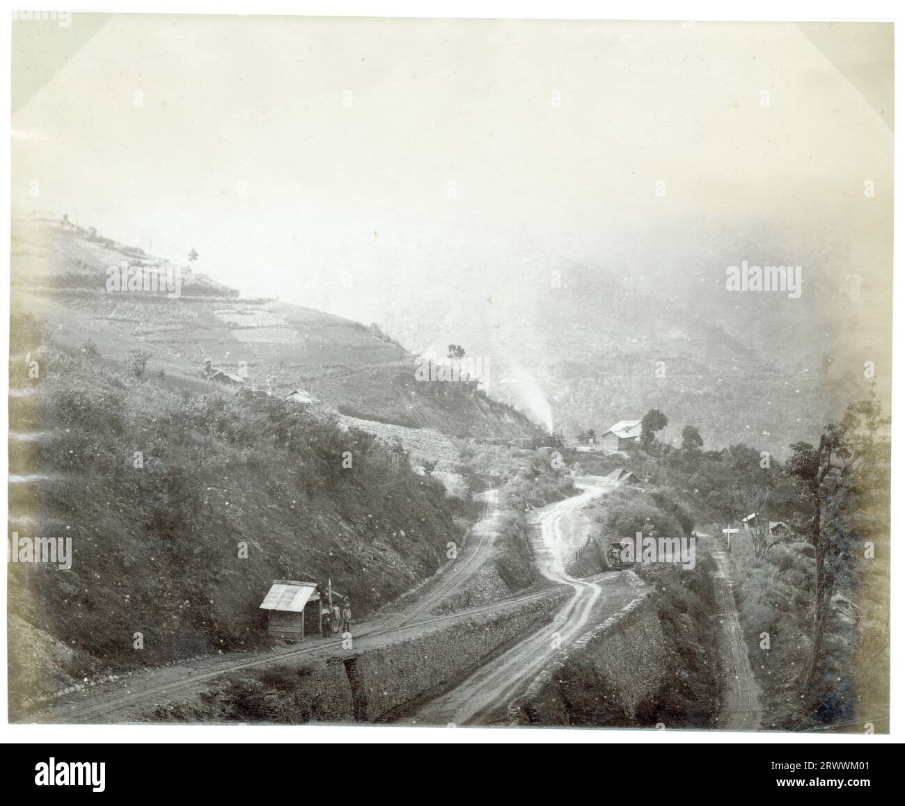 Vista della cima della collina con la ferrovia dell'Himalaya di Darjeeling. Piccoli edifici in legno possono essere visti sul lato della collina. Gruppi di persone stanno aspettando fuori da due delle capanne sul lato della linea ferroviaria. La didascalia recita: Darjeeling Himalaya Ry. Angolo di manovra doppio. Foto Stock