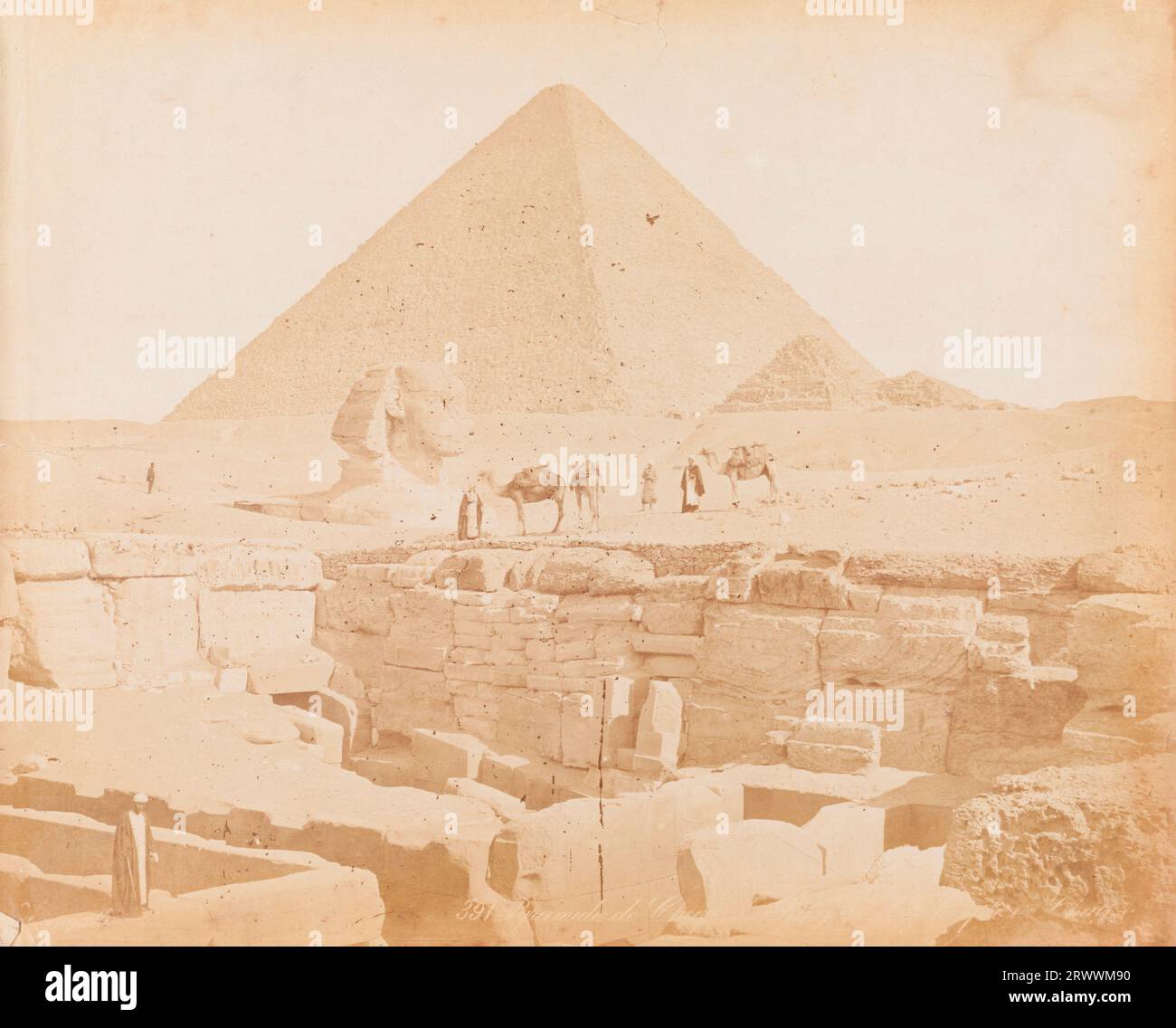 Vista della grande sfinge e delle piramidi di Giza. Accanto alla sfinge ci sono uomini egiziani in abito tradizionale che conducono tre cammelli. Il primo piano mostra le rovine delle tombe del tempio di Giza. Didascalia in negativo: 391 Pyramide de CH…[illeggibile]. Foto Stock