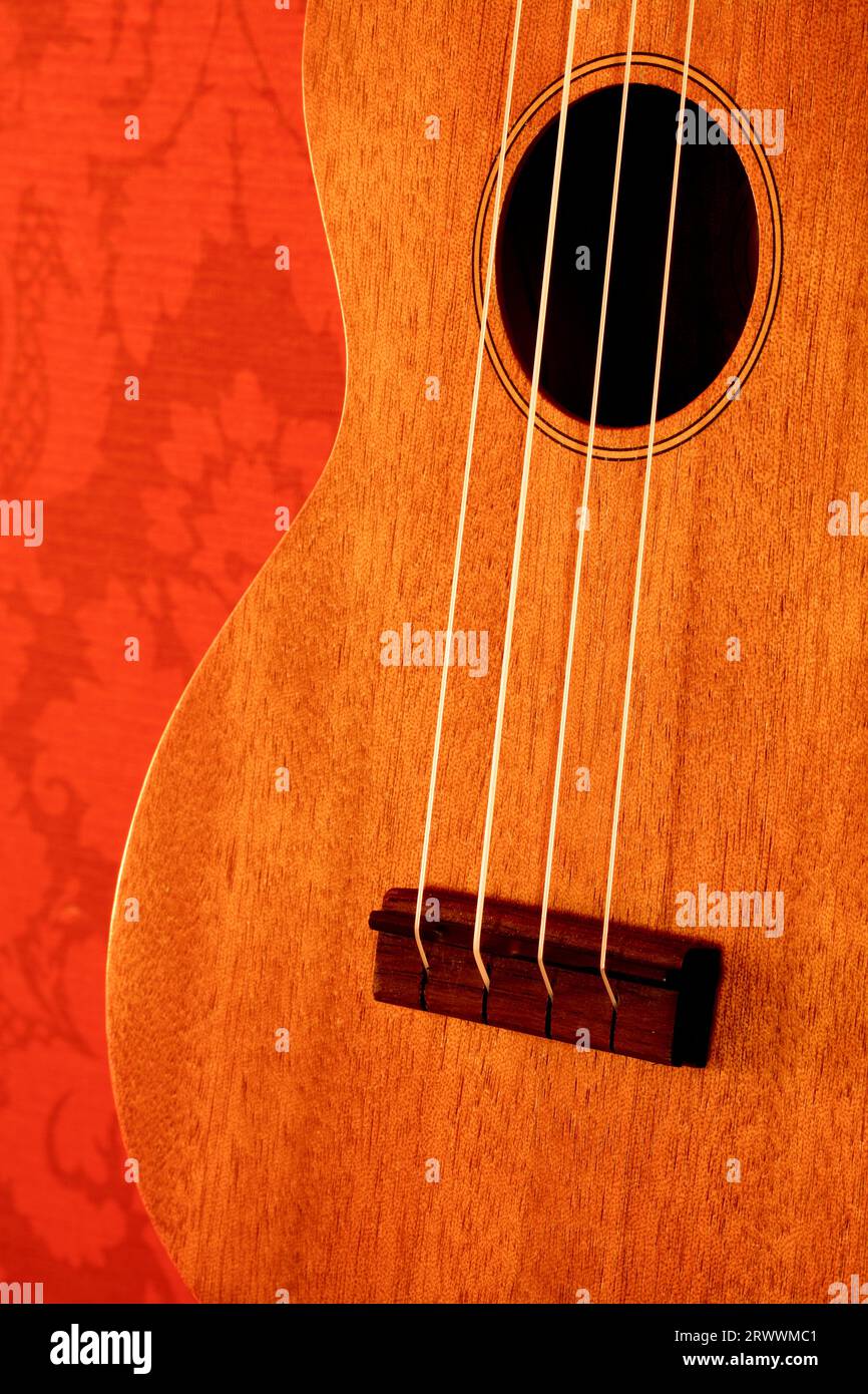 Un'immagine verticale del corpo di un ukulele su uno sfondo rosso con motivi. Foto Stock