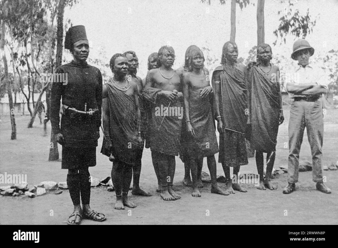 Un gruppo di otto giovani africani, probabilmente Maasai, si esibiscono in parata, indossando ancora indumenti tradizionali. Sono accompagnati da un soldato in uniforme africano che si trova all'attenzione e da un uomo europeo che si trova a suo agio. Didascalia del manoscritto originale: Raw Recruits K.A.R. B.E.A. Foto Stock