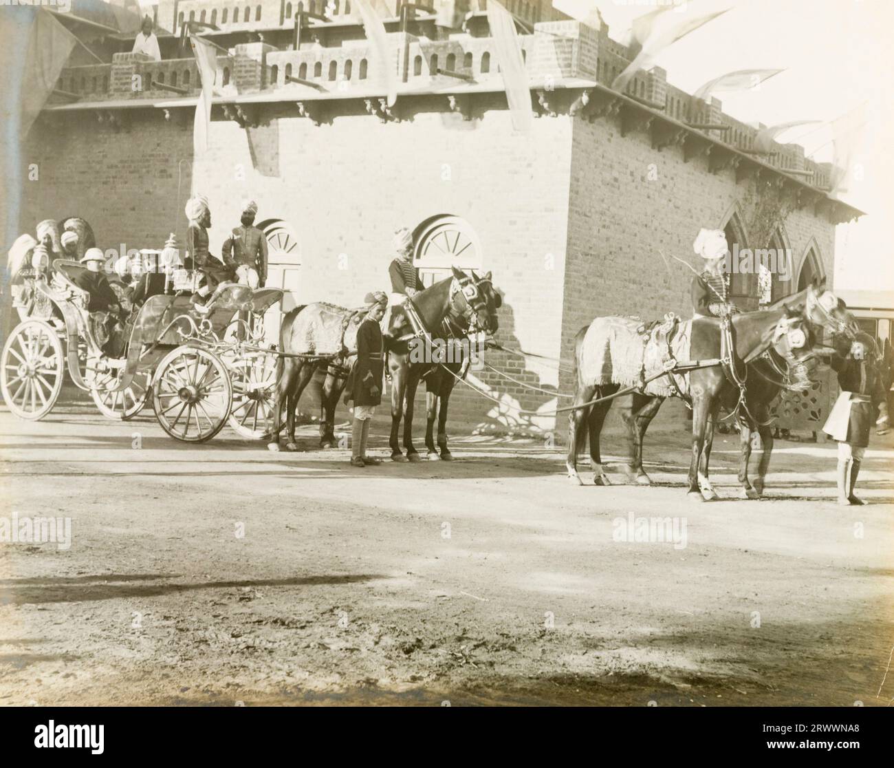 Quattro cavalli e i loro assistenti attendono istruzioni per tirare una carrozza con quattro funzionari del governo durante una processione, probabilmente all'installazione di Edward Maclagan come governatore del Punjab. Foto Stock