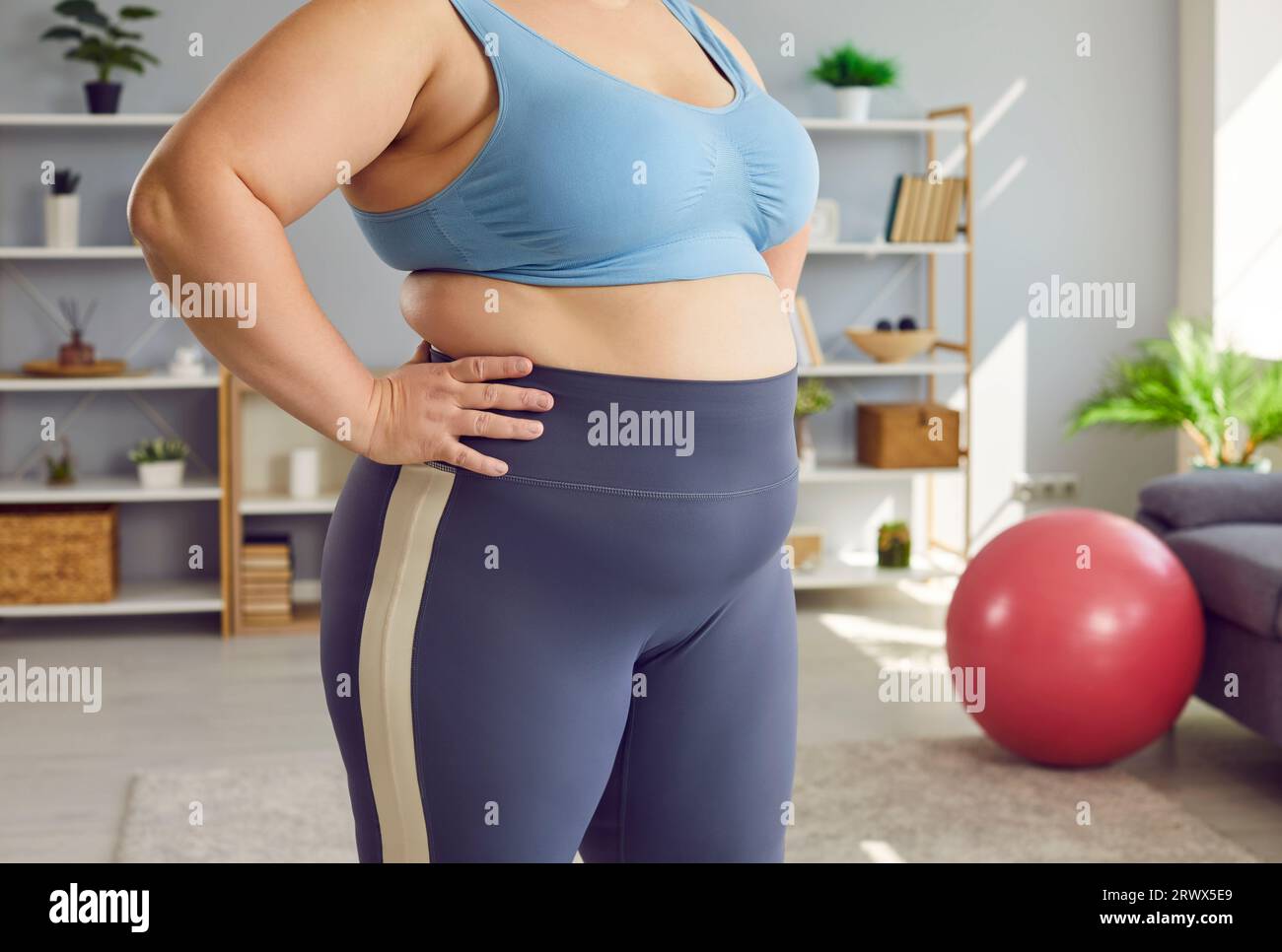 Ritratto ravvicinato ritagliato di una pancia e vita di una donna grassa in sovrappeso in piedi a casa. Foto Stock