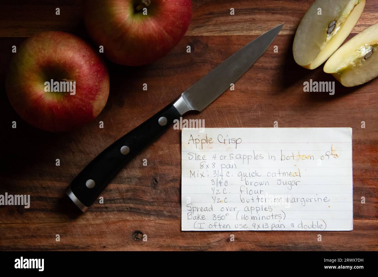 Scheda ricetta croccante di mele scritta a mano su tagliere di legno con coltello e mele Foto Stock