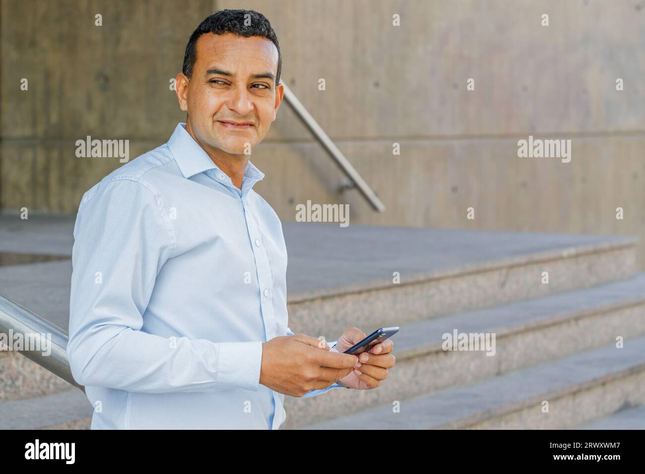 Giovane latinoamericano che usa un telefono cellulare sulle scale di un edificio con spazio per le copie. Foto Stock