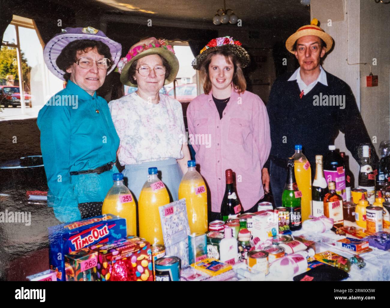 Tombola o bancarelle di bottiglie in un bazar di Pasqua al coperto con stallholder indossati con cofani pasquali, Inghilterra, Regno Unito Foto Stock