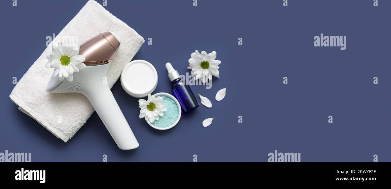 Fotoepilatore moderno, fiori, asciugamani e prodotti cosmetici su sfondo blu con spazio per il testo Foto Stock