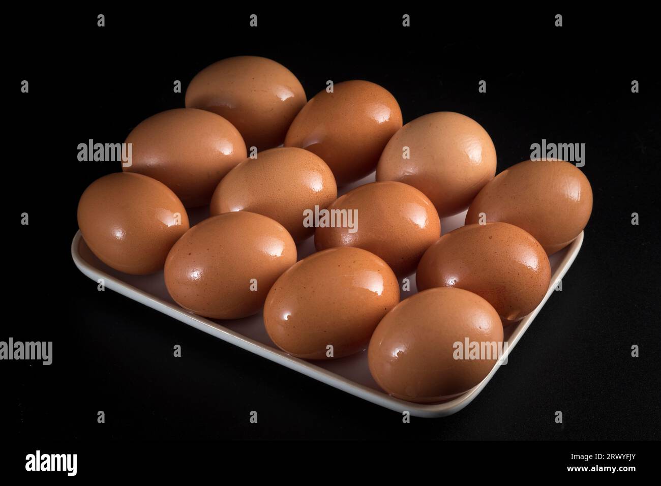 Una dozzina di uova poste su un vassoio bianco hanno una notevole umidità e si distinguono in modo significativo sullo sfondo nero. Foto Stock