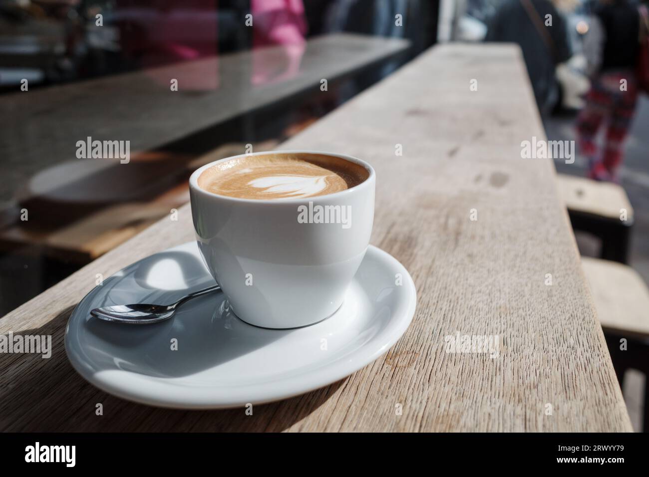 Messa a fuoco selezionata e vista ravvicinata di una tazza di cappuccino in ceramica bianca sulla parte superiore con una bella latte art delicata con motivo a cuore, su legno all'aperto. Foto Stock