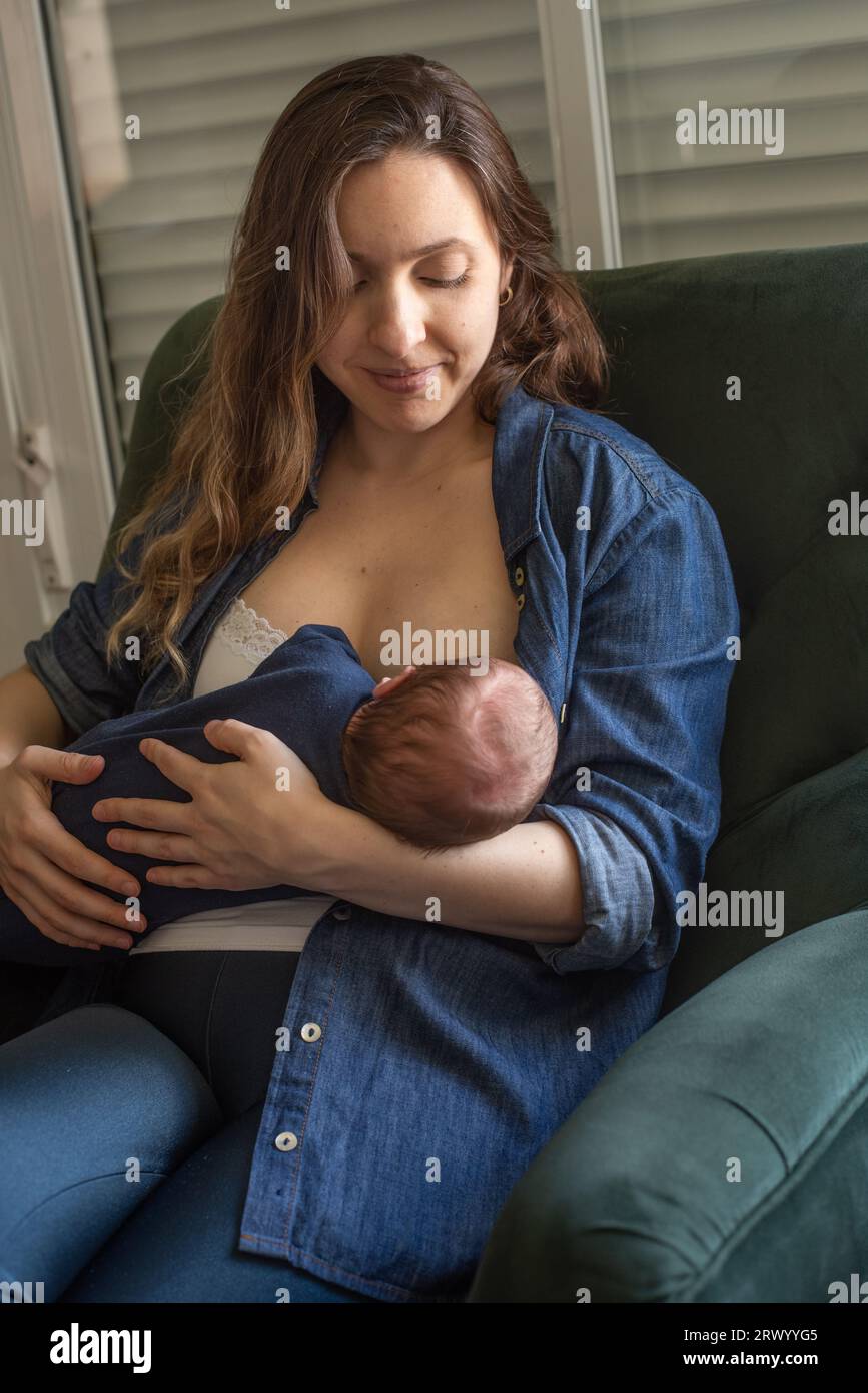 Madre brasiliana che allatta il bambino mentre è seduta sulla poltrona a casa Foto Stock