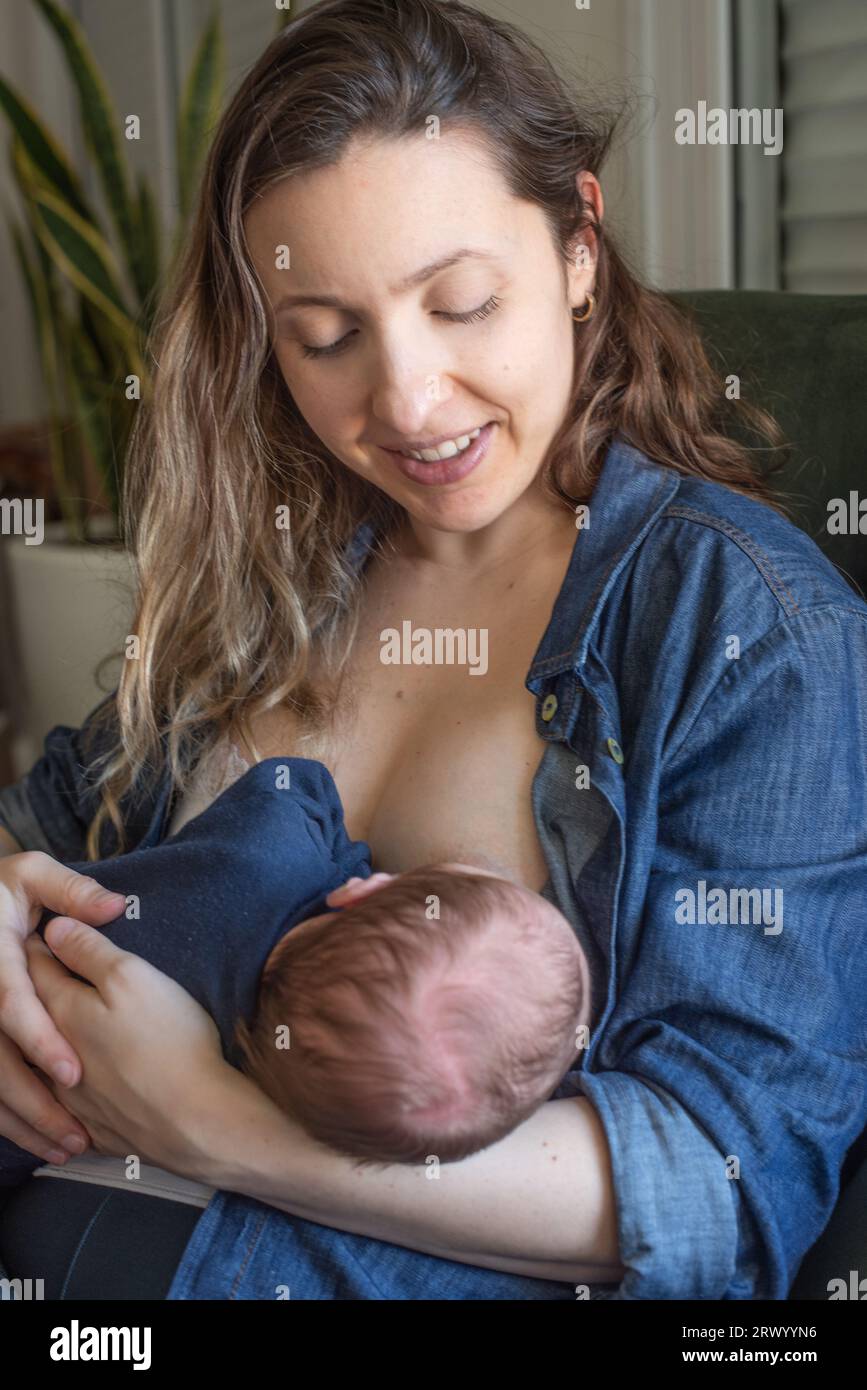 Mamma felice che allatta il bambino mentre è seduto sulla poltrona a casa Foto Stock