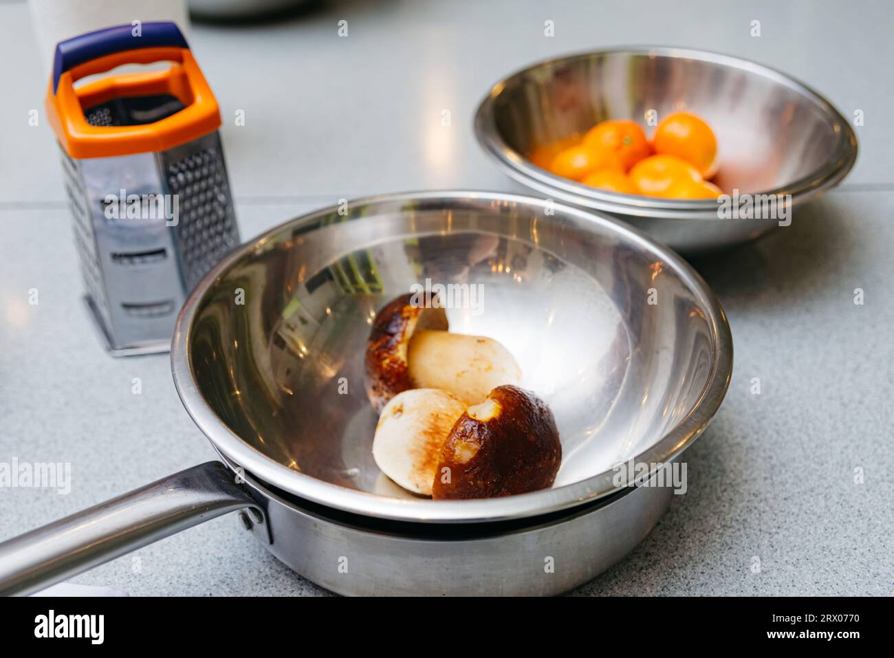 un set di utensili da cucina prima di cucinare, ciotole in acciaio  inossidabile, una grattugia e funghi porcini scongelati, una padella  metallica su un tavolo da cucina Foto stock - Alamy