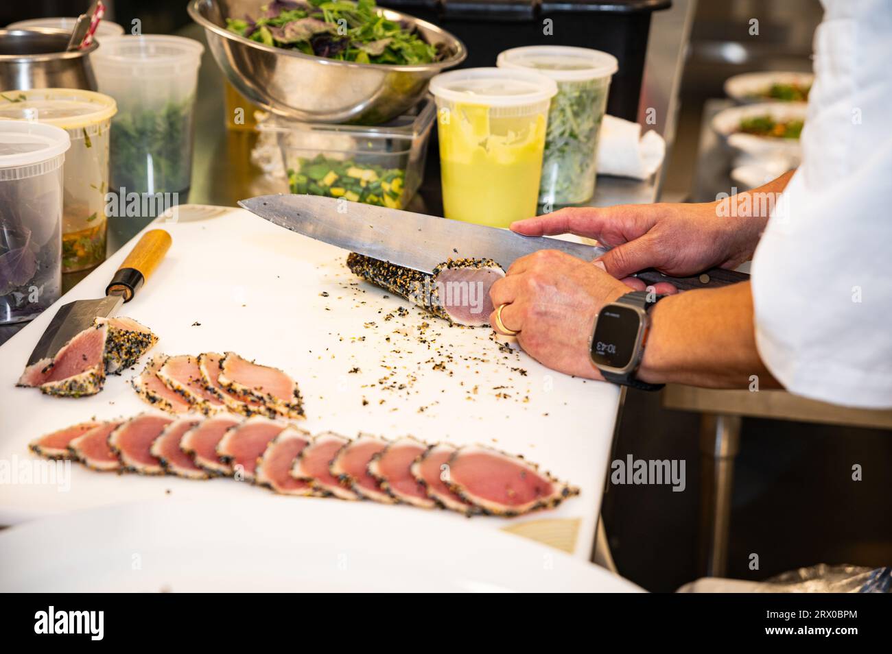 Foto delle braccia di un uomo in una cucina commerciale che affetta tonno albacora in crosta di furikake Foto Stock