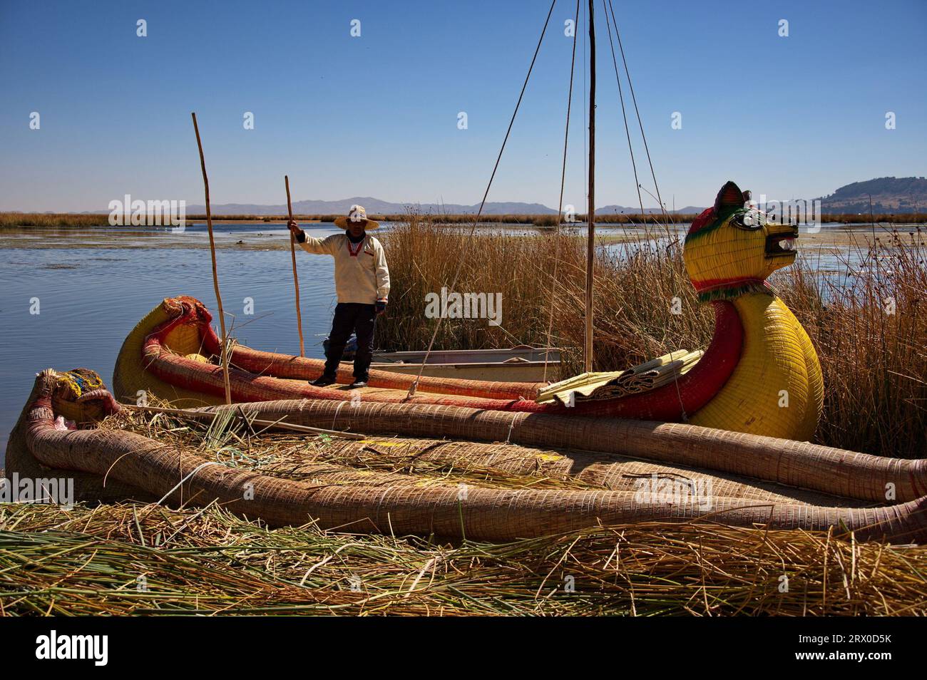 Un uomo di Uros in piedi su una barca di canne vicino alla sua isola galleggiante sul lago Titicaca Foto Stock