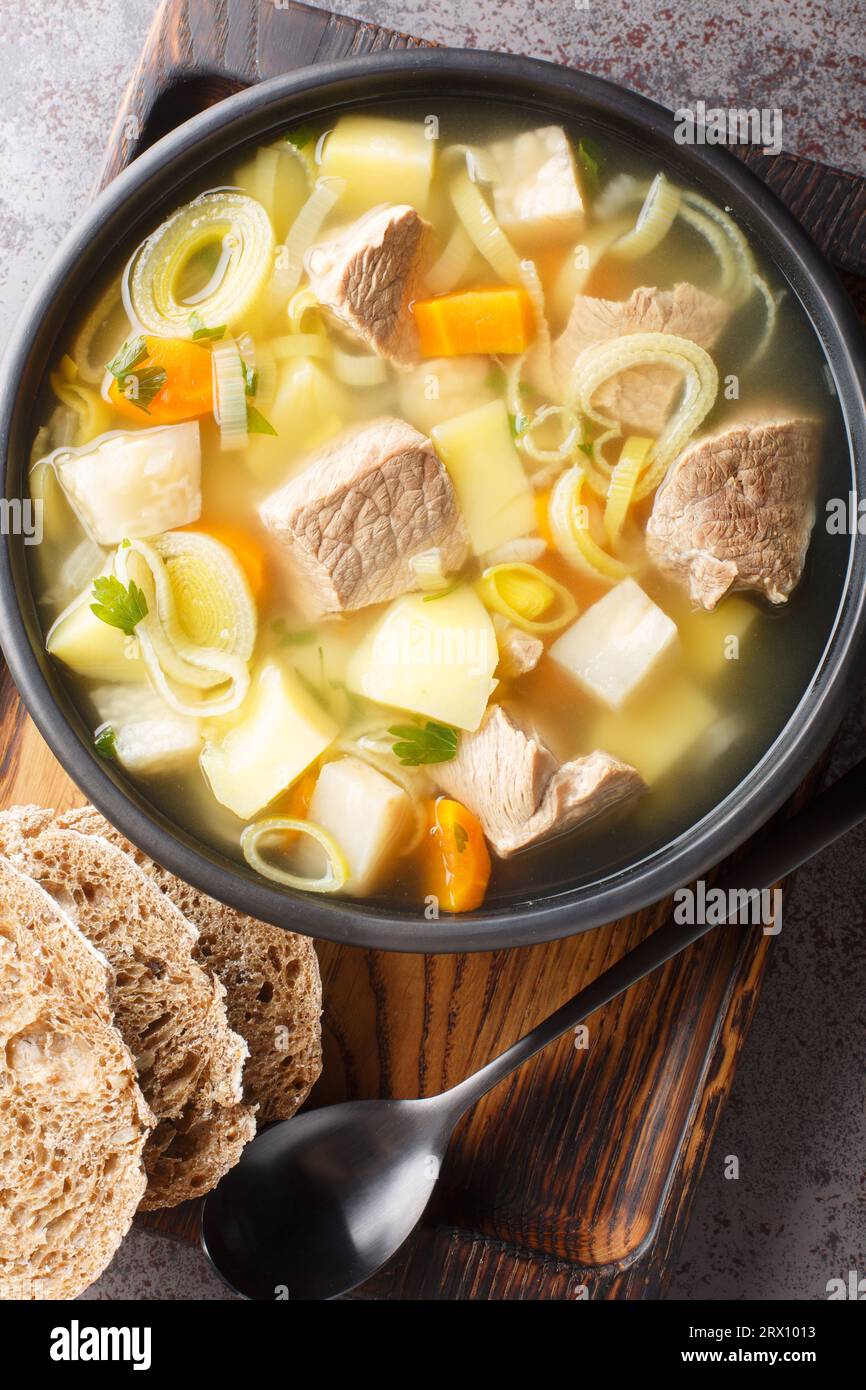 Deliziosa zuppa di vitello, patate, carote, porri, sedano e pastinaca da vicino in un piatto sul tavolo. Vista dall'alto verticale Foto Stock