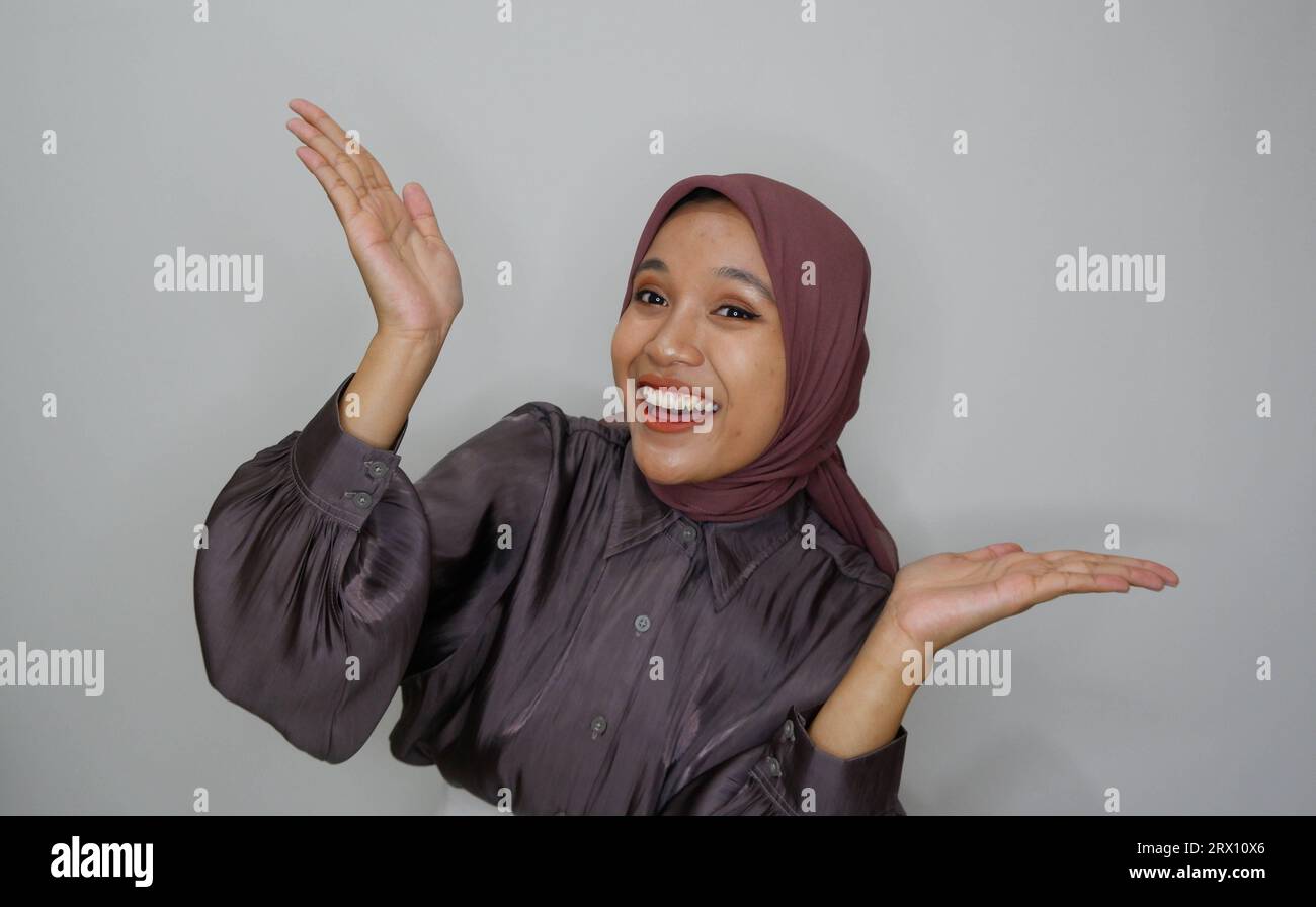 Giovane bella donna musulmana asiatica che indossa un velo grida e urla forte con una mano sulla bocca. concetto di comunicazione. Foto Stock
