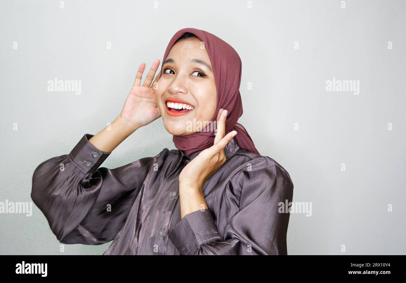 Giovane bella donna musulmana asiatica che indossa un velo grida e urla forte con una mano sulla bocca. concetto di comunicazione. Foto Stock