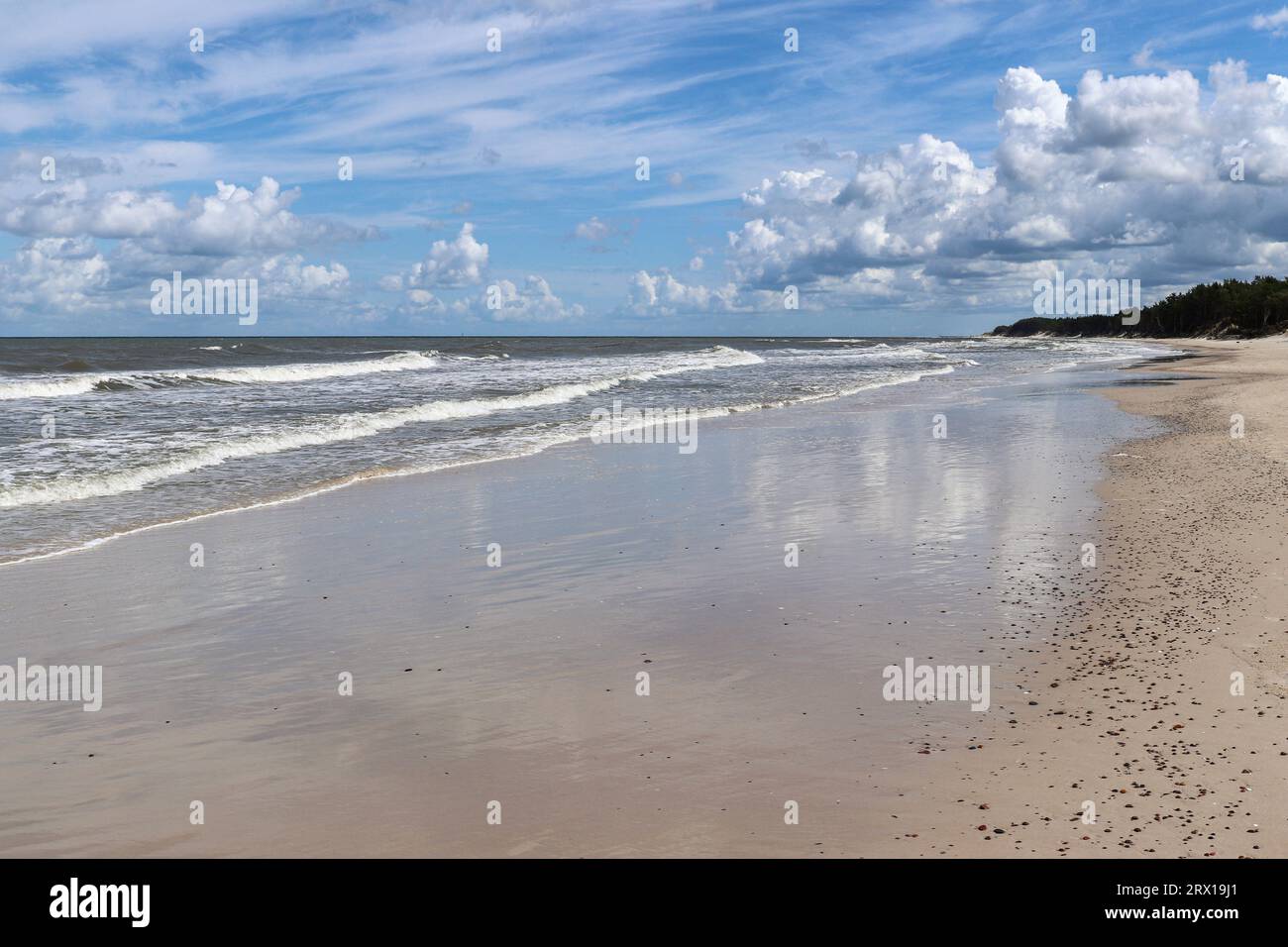 Cielo blu e nuvole bianche riflesse nella sabbia bagnata di una spiaggia sulla costa del Mar Baltico in Polonia Foto Stock