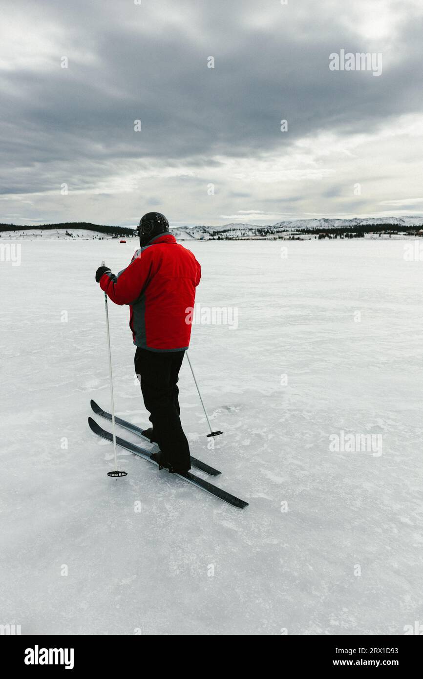 Uomo con cappotto rosso per lo sci di fondo nel cielo nuvoloso sul lago ghiacciato Foto Stock