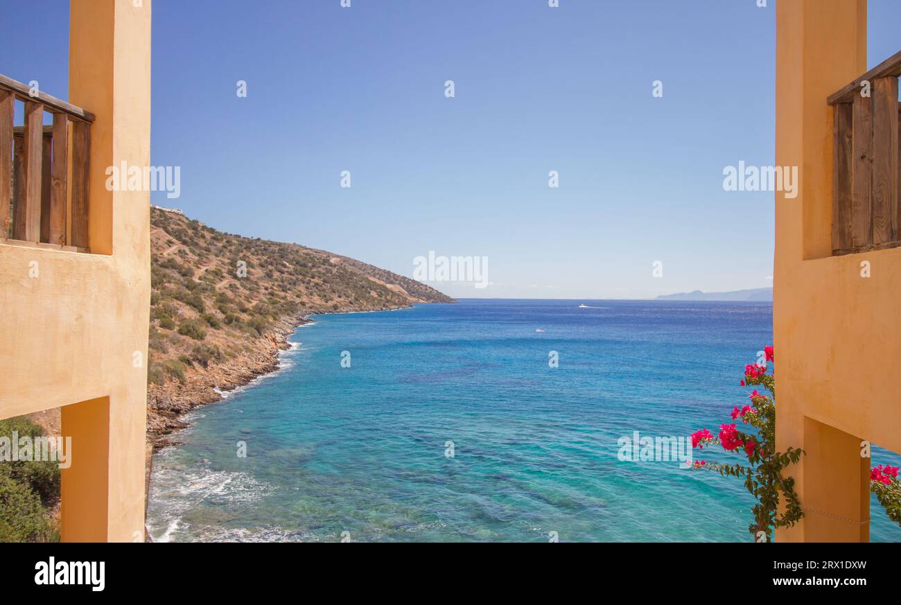 Vista del mare turchese del mediterraneo sull'isola di Creta, Grecia, con edifici tradizionali e fiori, vicino ad Agios Nikolaos Foto Stock