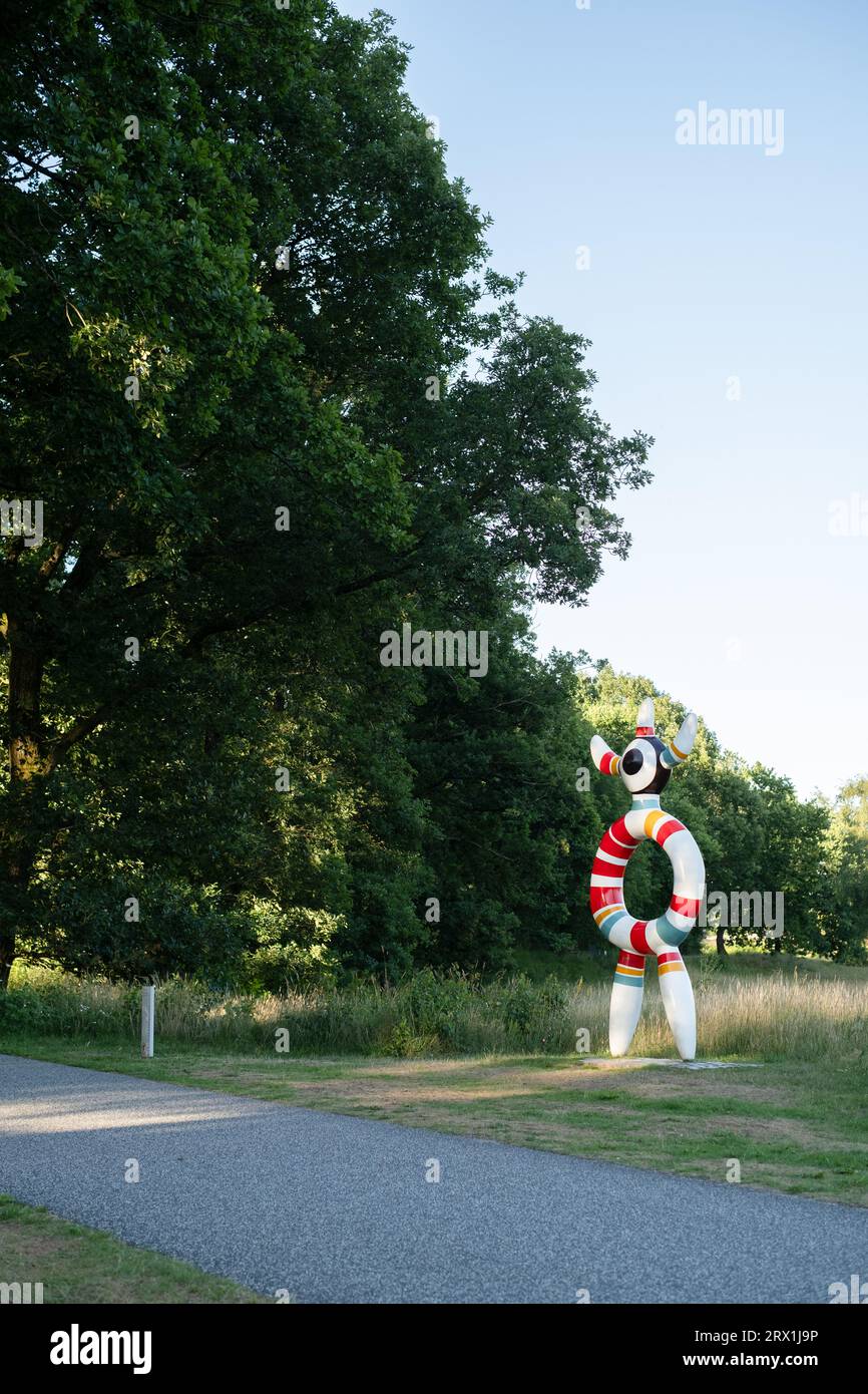 Skulpturpark Billund, Danimarca, come il tramonto, con una scultura colorata a destra, alberi a sinistra e un sentiero pavimentato in primo piano. Foto Stock